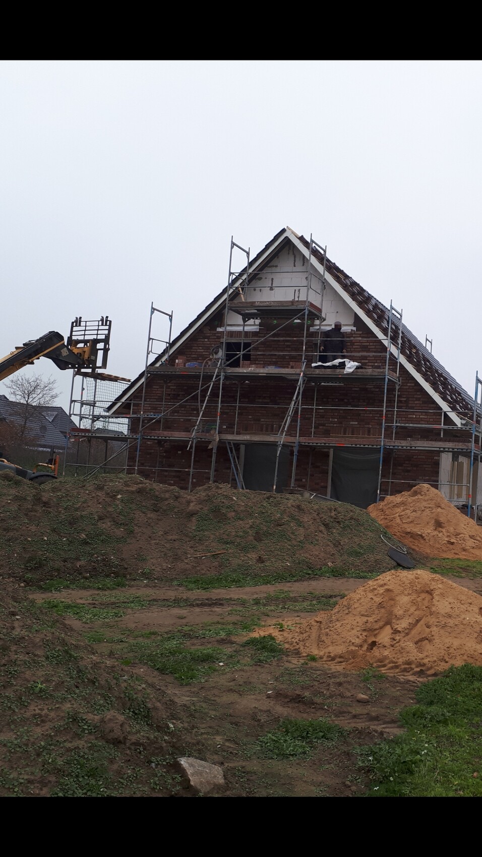 Haus im Rohbau mit Gerüst, Ziegelwand, Sandhaufen und Baugerät auf der Baustelle.