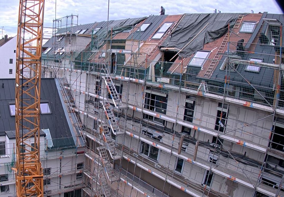 Baustelle: mehrstöckiges Gebäude mit Gerüst, Kran und Dacharbeiten; Arbeiter auf dem Dach.