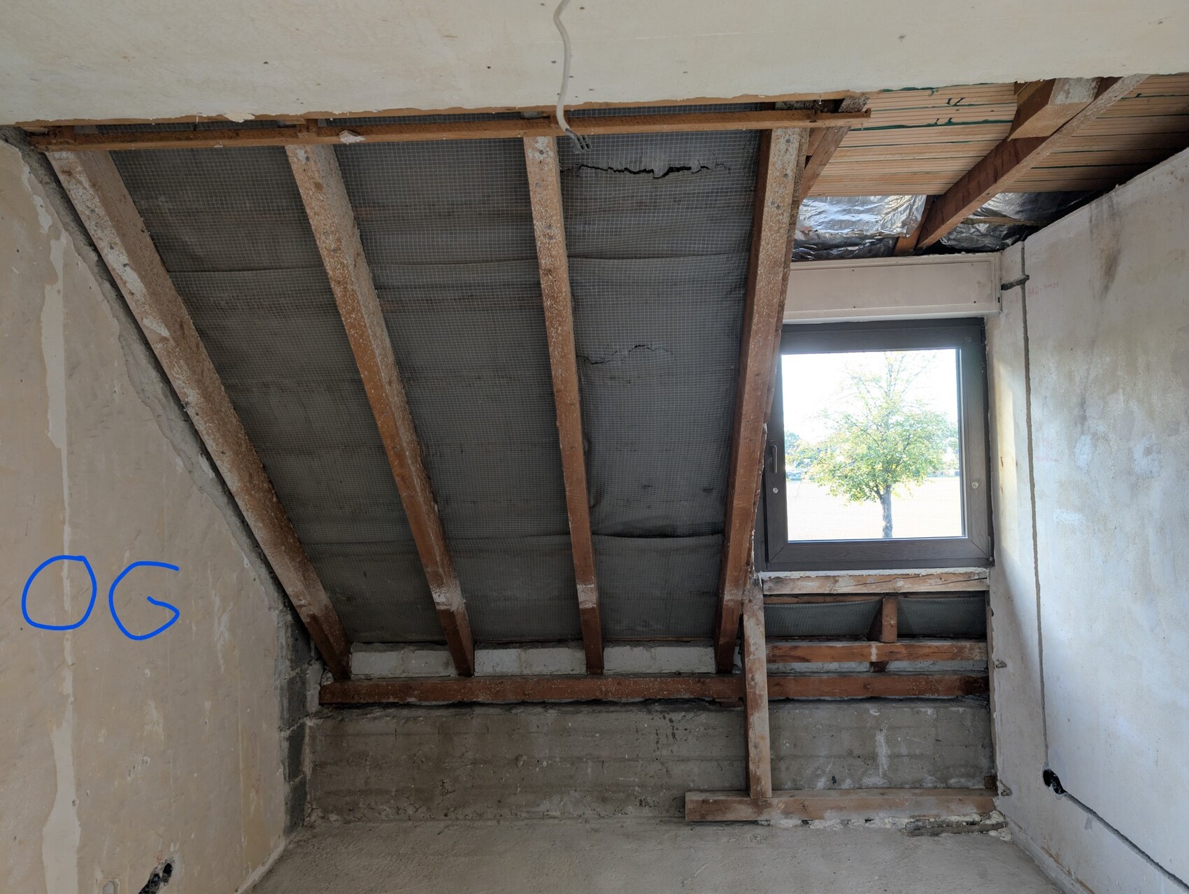 Unverkleideter Dachboden mit Holzbalken, Dämmung und Fenster im Rohbau