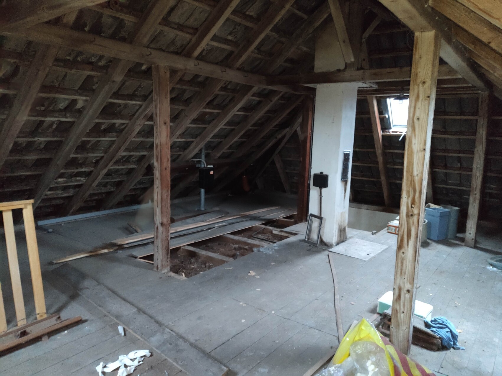 Unfertiger Dachboden mit Holz-Dachstuhl, weißer Stütze, Dachfenster rechts, Baumaterialien.