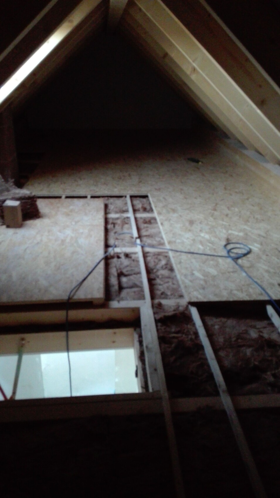 Dachgeschoss-Rohbau mit Dachstuhl, Dämmung und sichtbaren Kabeln.