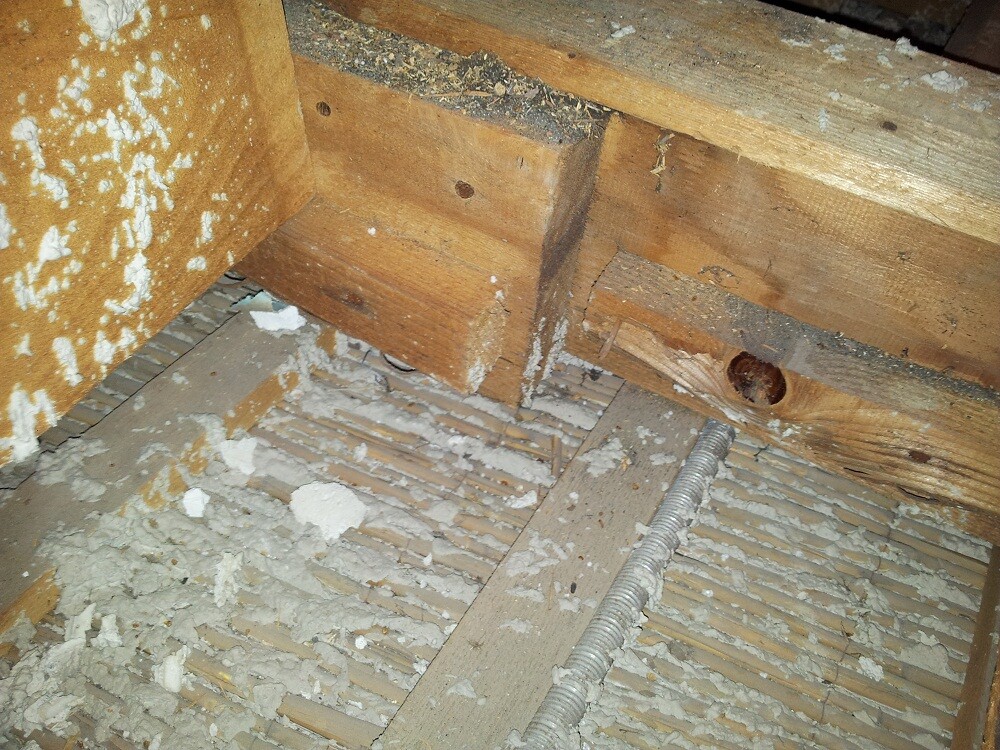 Unbearbeitetes Dachgeschoss mit Holzbalken, Dämmmaterialreste und Rohrleitung auf dem Boden