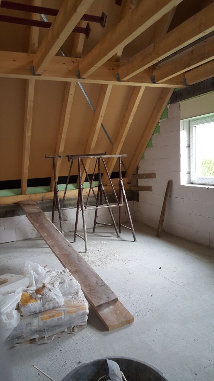 Dachgeschoss-Bauzimmer mit Holzbalken, Gerüst, Holzbohlen und Baumaterial.