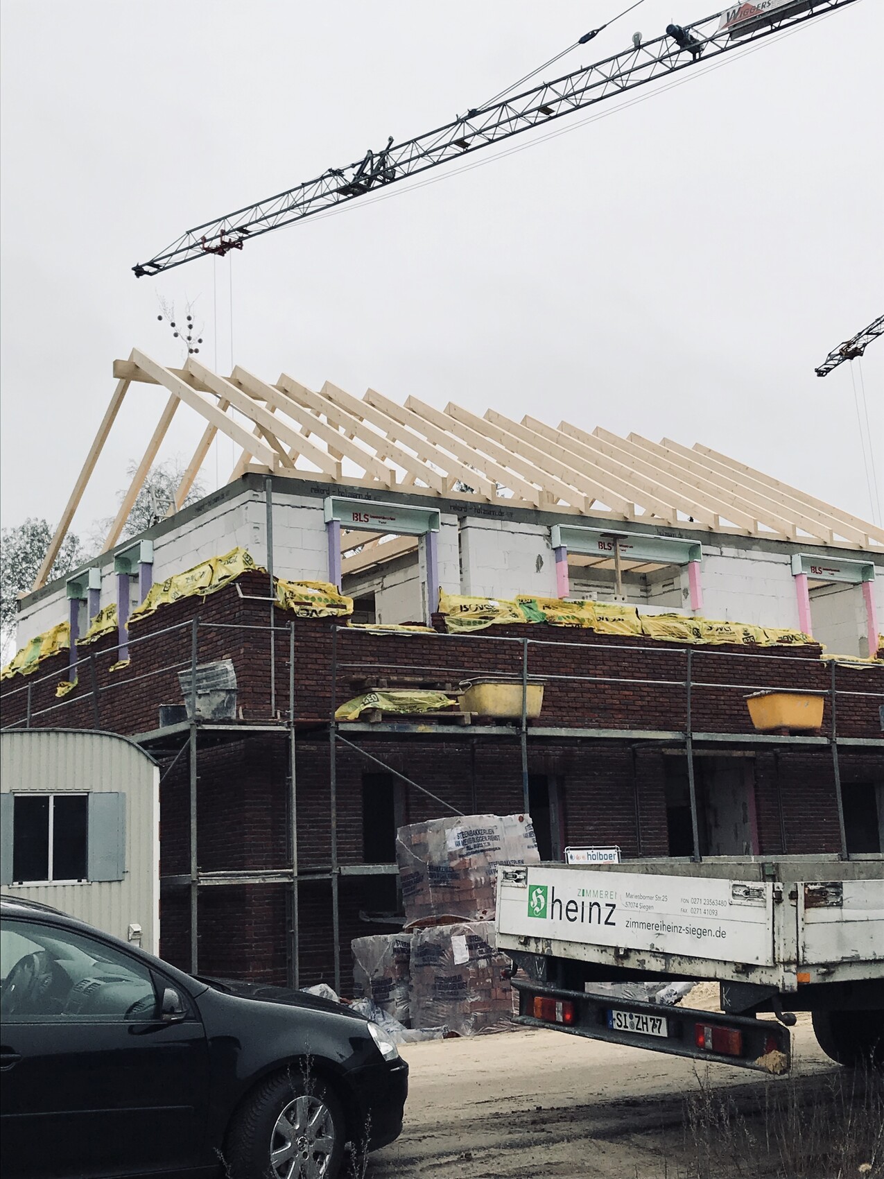 Baustelle mit Kran und Holzdachkonstruktion auf Rohbau eines Gebäudes.