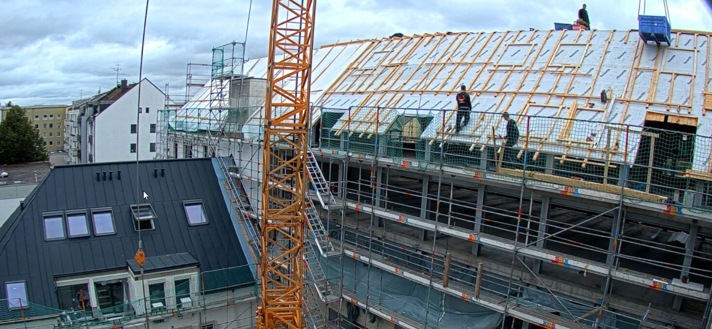 Bauarbeiter montieren Dachkonstruktion auf einer Baustelle mit Gerüst und Kran im Vordergrund.