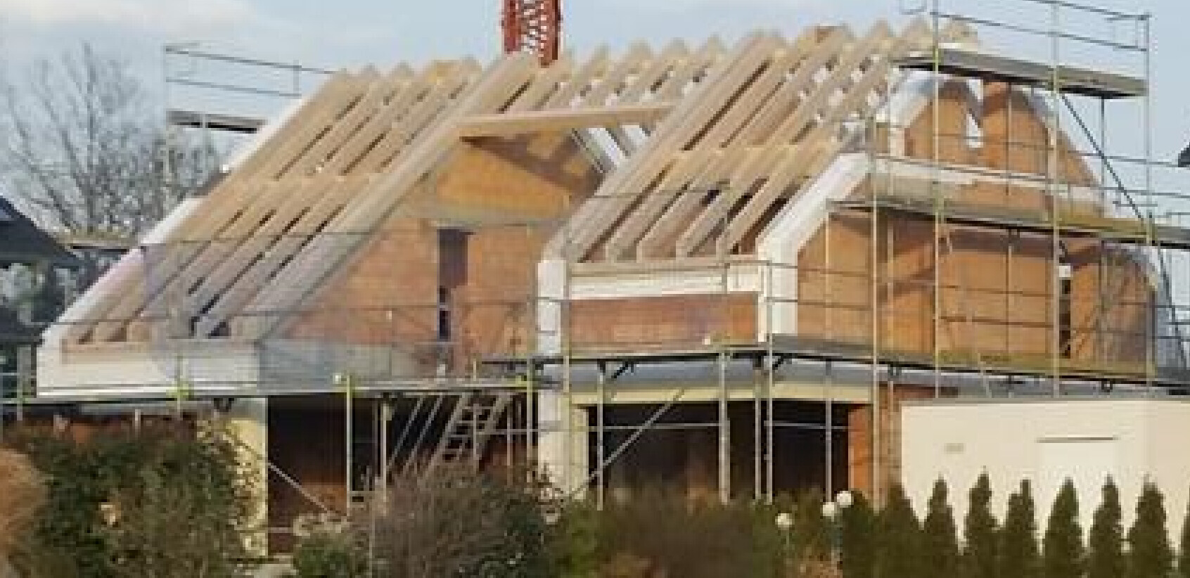 Rohbau eines Hauses mit sichtbarem Dachstuhl und Gerüst auf der Baustelle