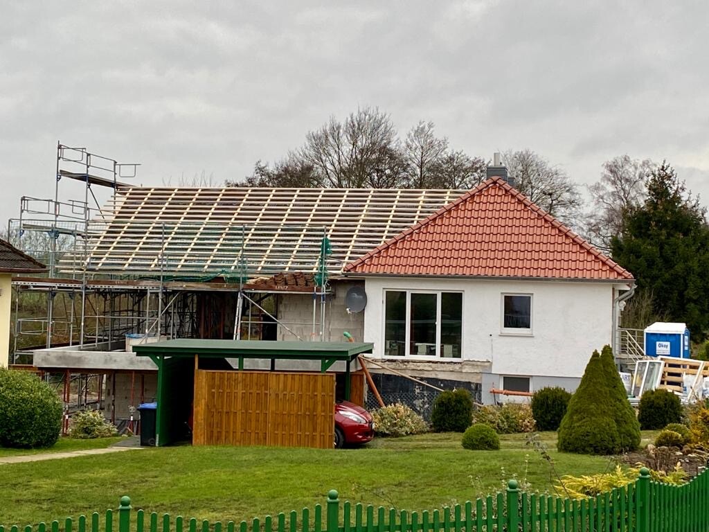 Einfamilienhaus im Rohbau mit Gerüst, Dachkonstruktion und Gartenbereich.