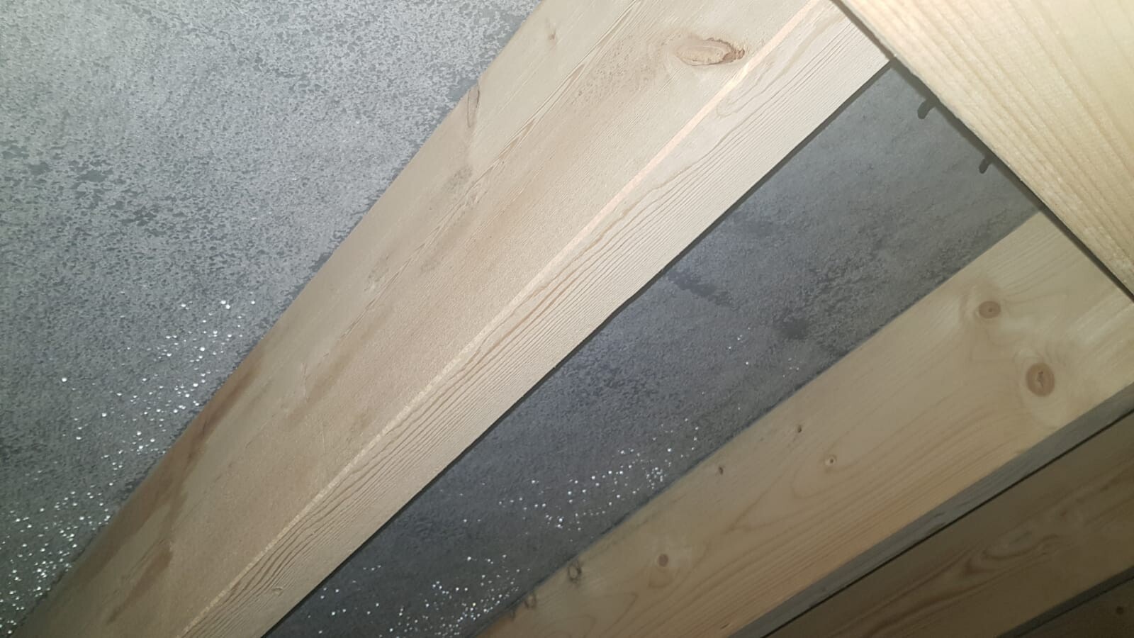 Diagonal angeordnete Holzbalken vor grauer Betonwand; Baukonstruktion.