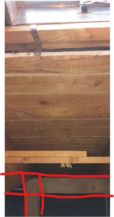 Holzdecke mit Holzbalken, Metallband und rote Markierungen am unteren Rand des Bildes