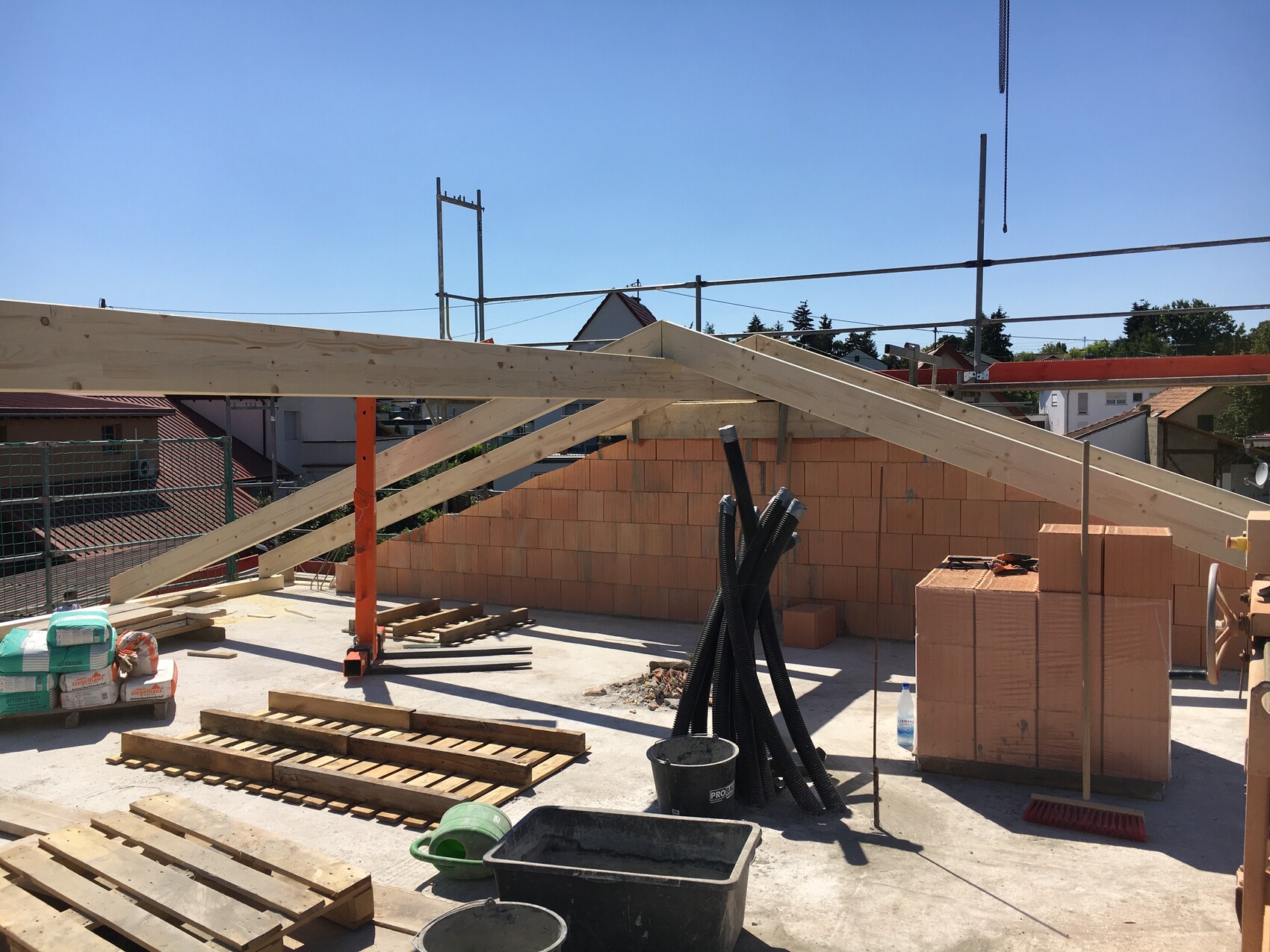 Baustelle mit Holzdachkonstruktion, Backsteinmauer, Rohre, Paletten und Eimer.
