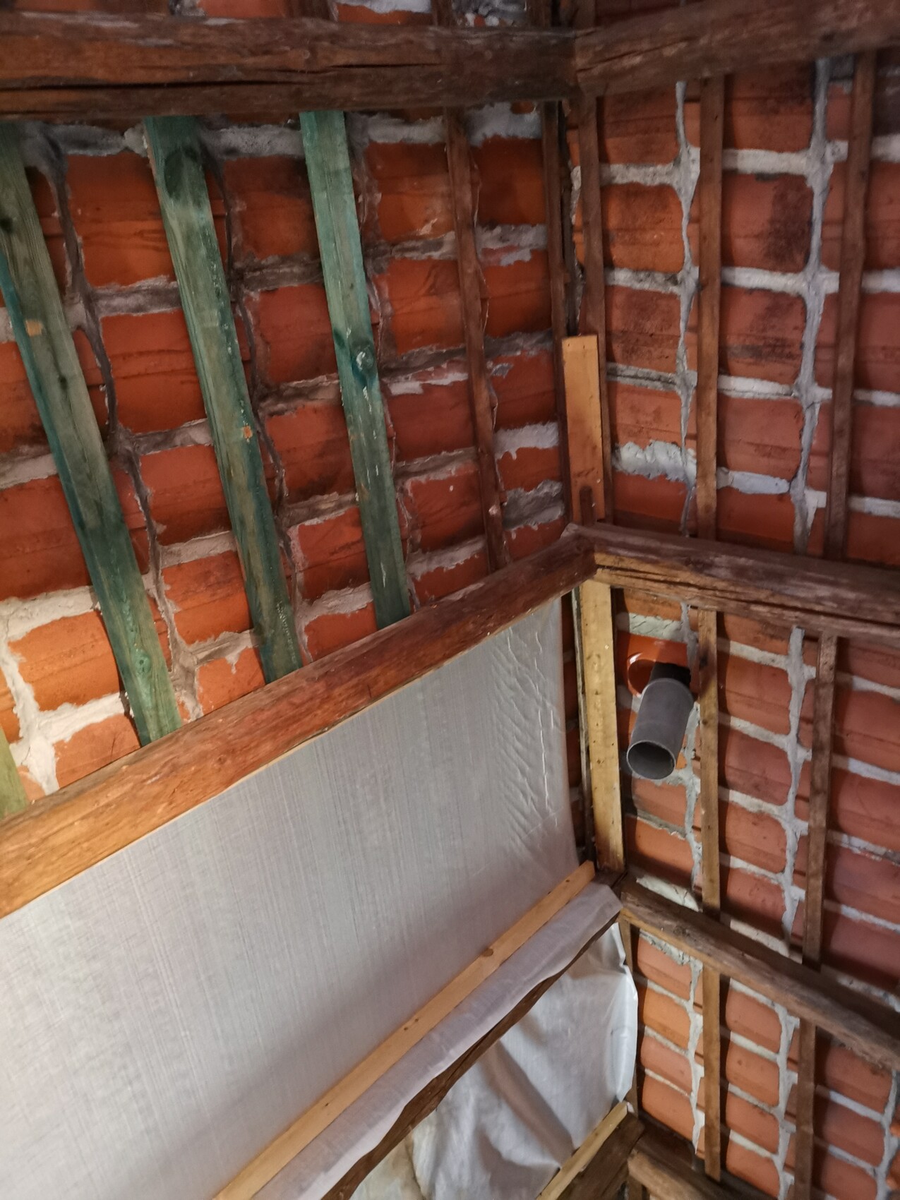 Dachboden mit roten Ziegeln, Holzbalken, grün gestrichenen Latten und einer Rohrleitung.