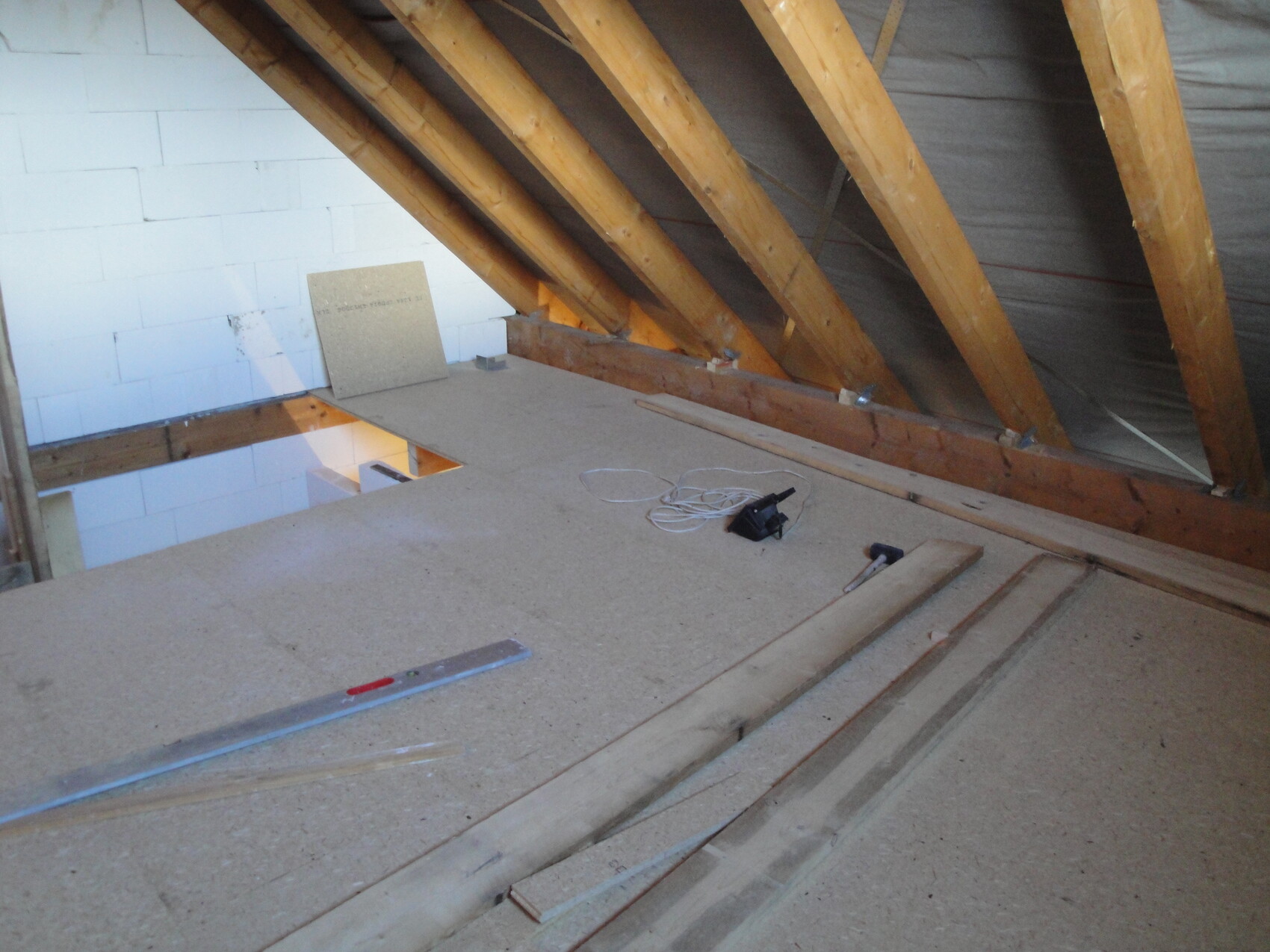 Dachboden-Rohbau: sichtbare Holzbalken, OSB-Boden, Dämmplatten und Werkzeuge.