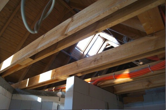 Rohbau mit sichtbaren Holz-Dachstuhlträgern, Dachöffnung und Installationen