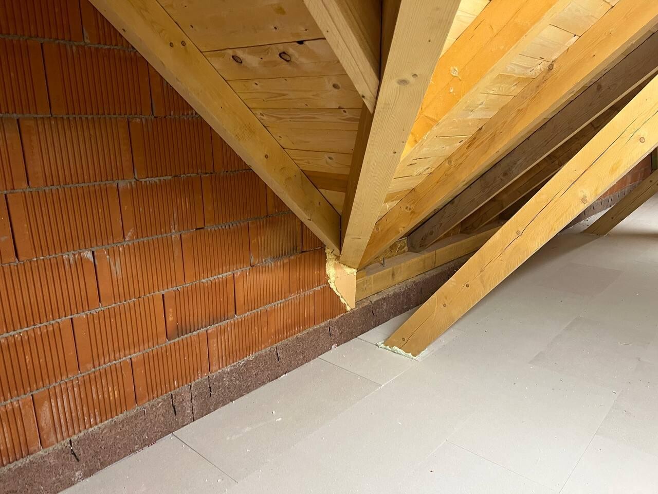 Dachboden mit Holzbalken, roter Ziegelwand und Fliesenboden.