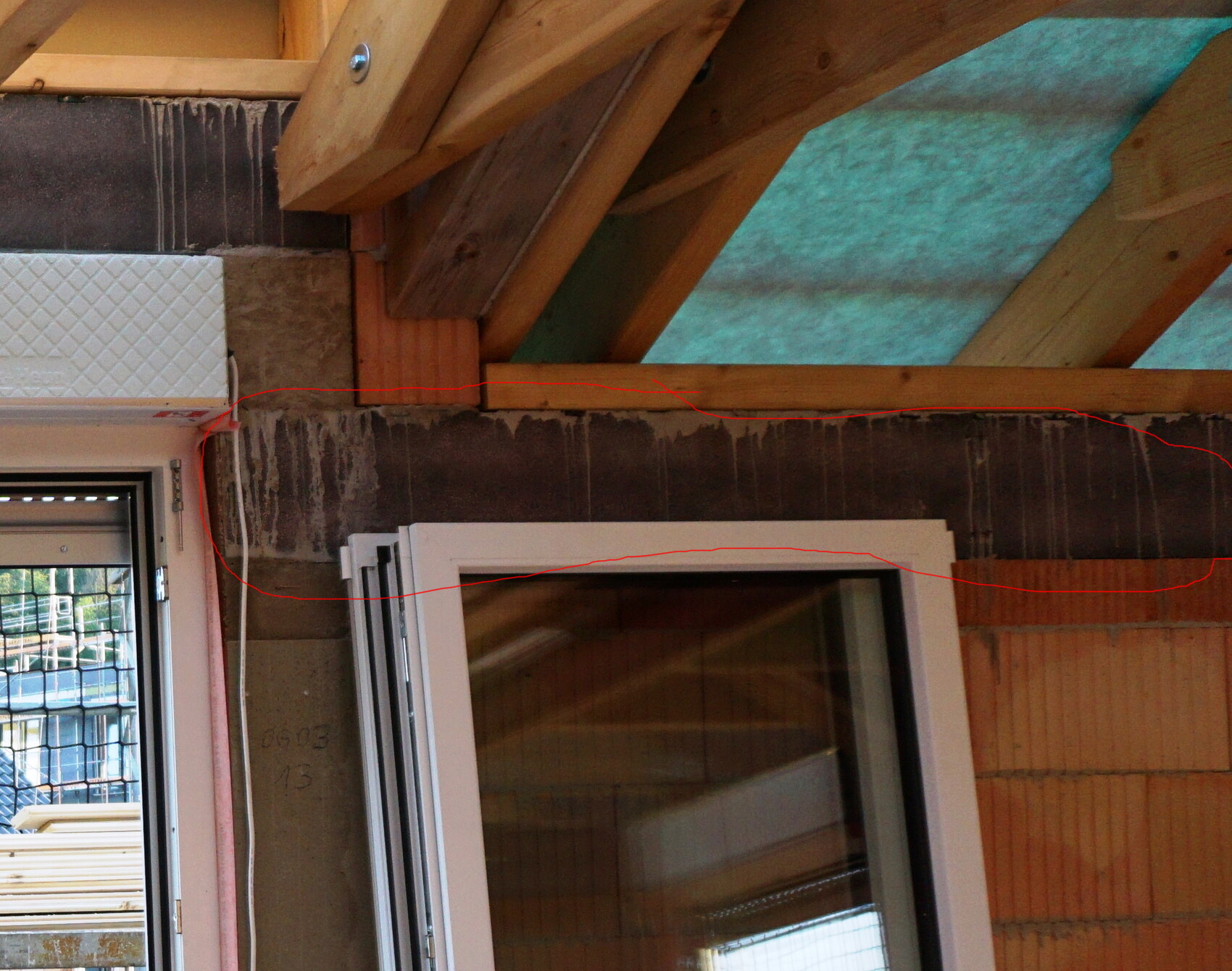 Rohbau-Wand mit Fensterrahmen, sichtbare Holz-Dachkonstruktion und Dämmmaterial.