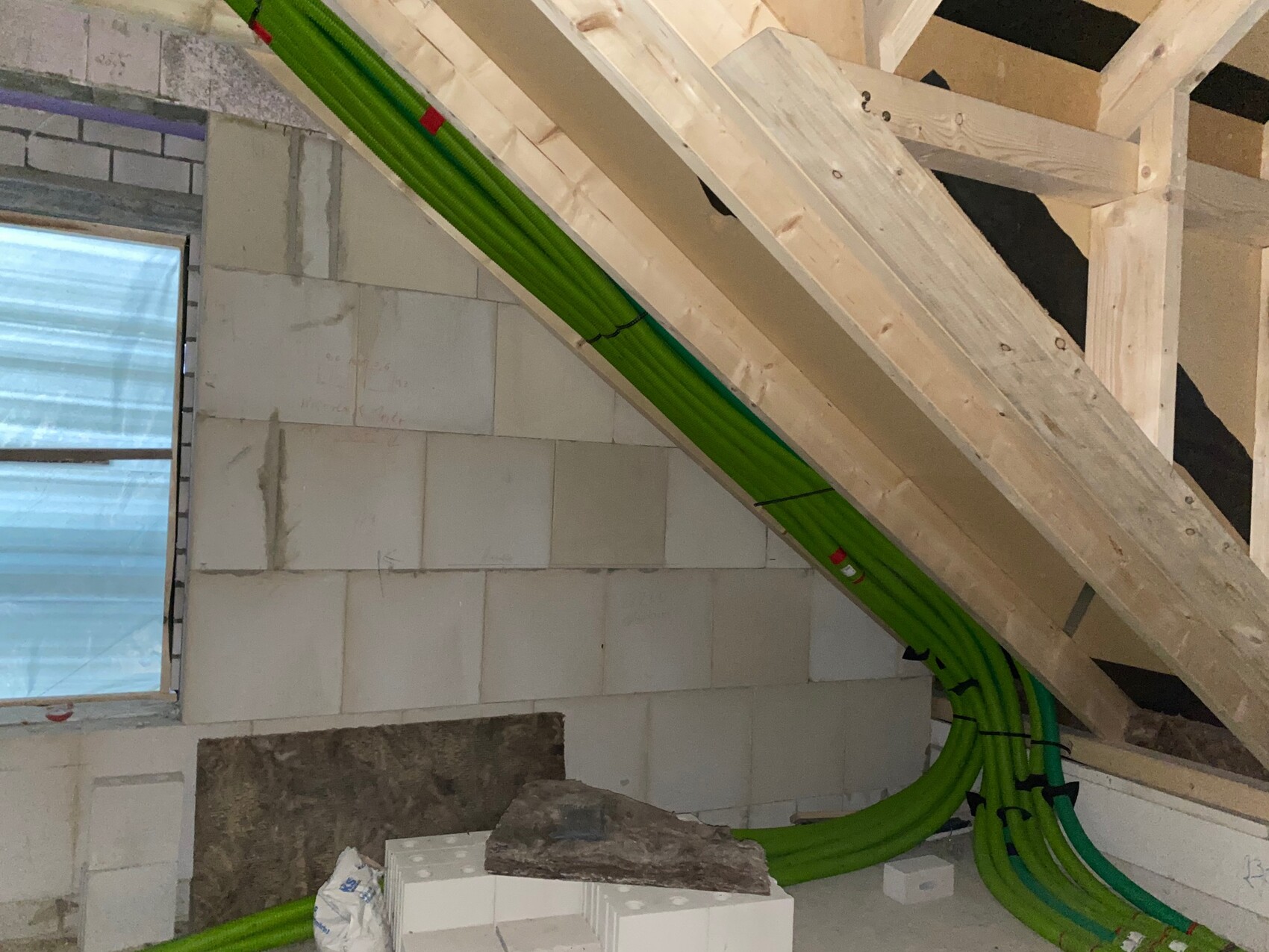 Innenraum einer Baustelle mit grünen Rohrleitungen, die unter Holzbalken entlang einer Wand verlaufen.