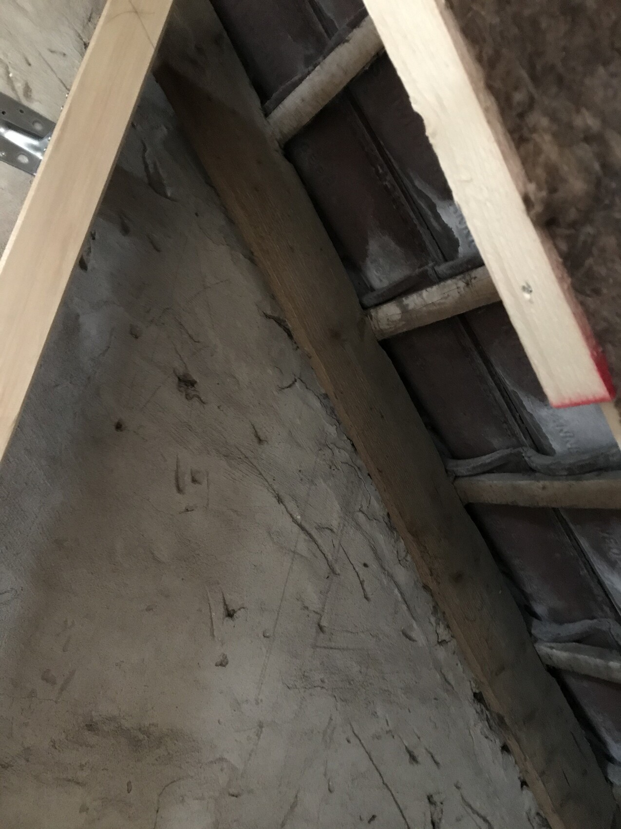 Dachboden-Rohbau mit Holzbalken, staubiger Wand und sichtbaren Dachlatten.