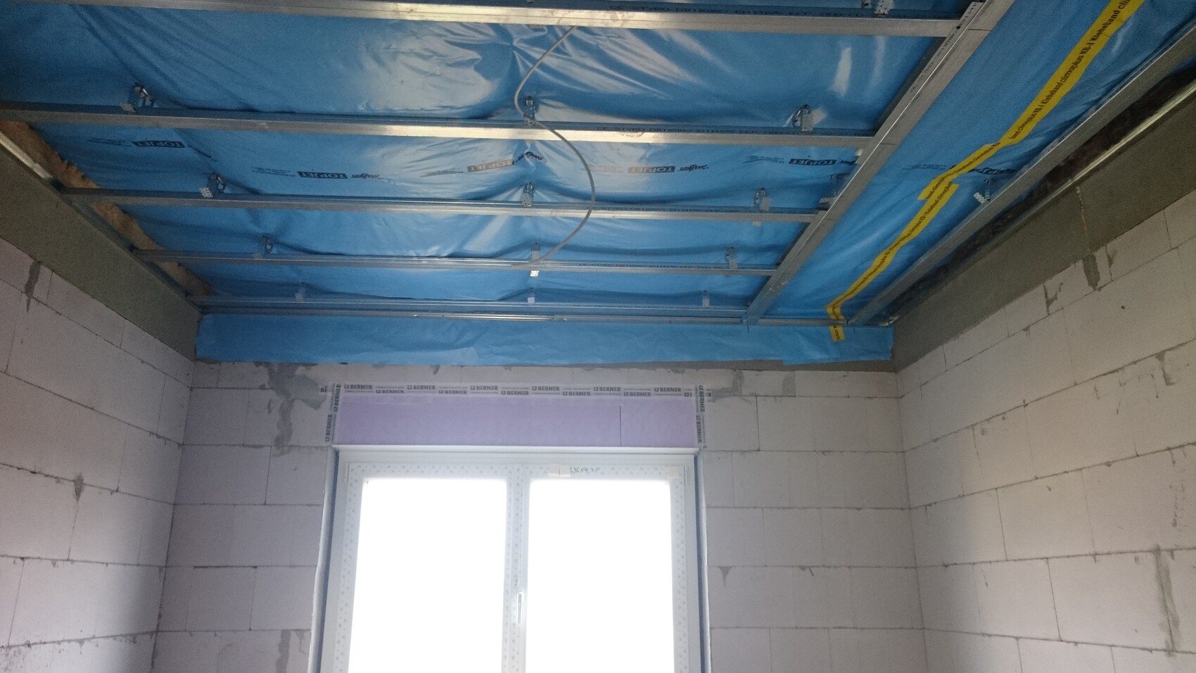 Baustelle: offener Deckenbereich mit blauer Abdeckung, Stahlträgern und Fenstern
