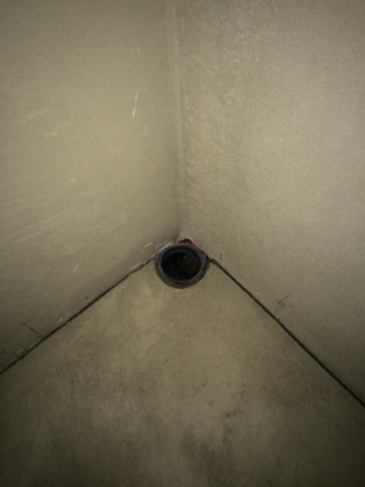 Ecke eines rauen Betonraums mit runder Rohröffnung im Boden zwischen zwei Wänden.