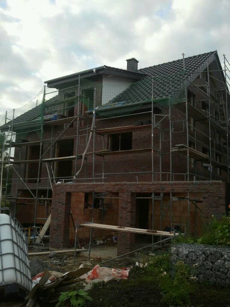 Mehrstöckiges Haus im Bau mit Metallgerüst, rote Ziegelwände und Bauutensilien.