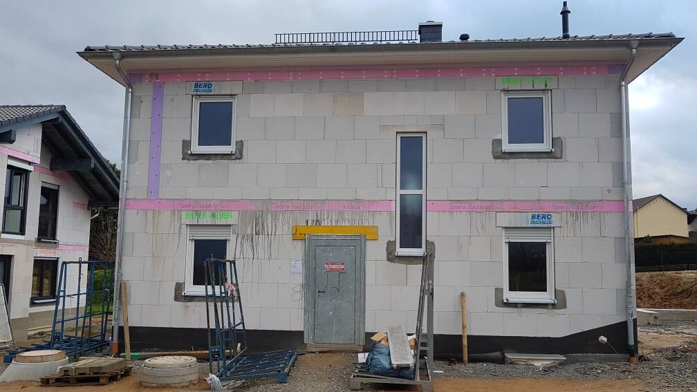 Zweistöckiges Haus im Rohbau mit Isolierplatten, Fenstern, Tür und Baugeräten.