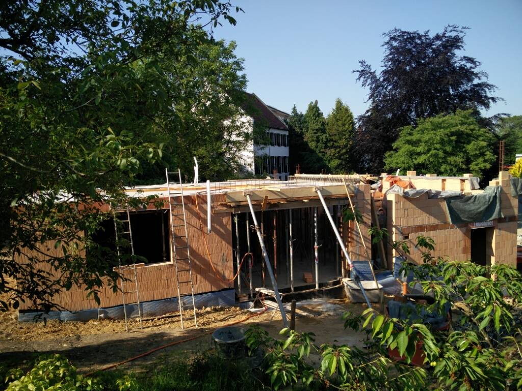 Rohbau eines Einfamilienhauses mit Ziegelwänden, Gerüst und Bauarbeiten im Garten