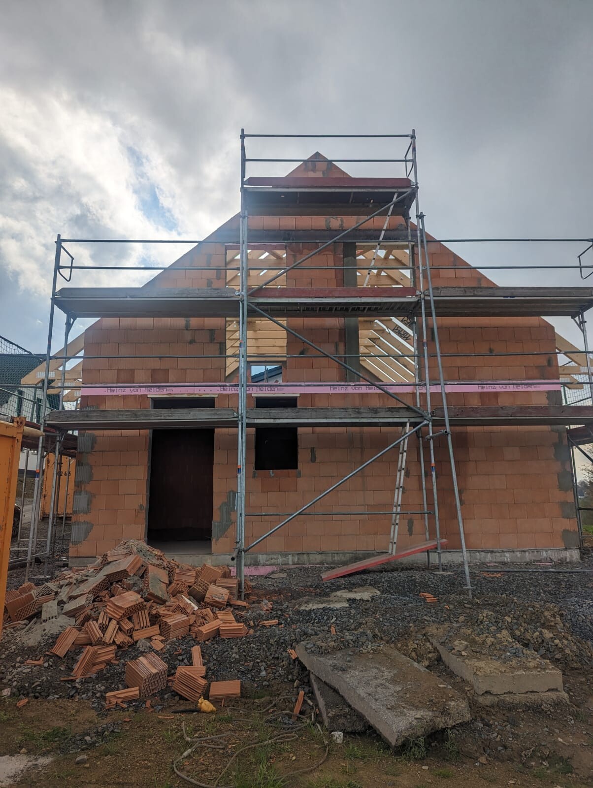 Rohbau eines roten Ziegelhauses mit Gerüst; Fensteröffnungen, Ziegelsteine liegen am Boden.