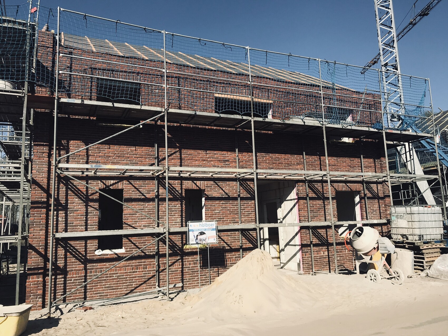 Rohbau eines Hauses mit Gerüsten, Sandhaufen und Betonmischer auf Baustelle