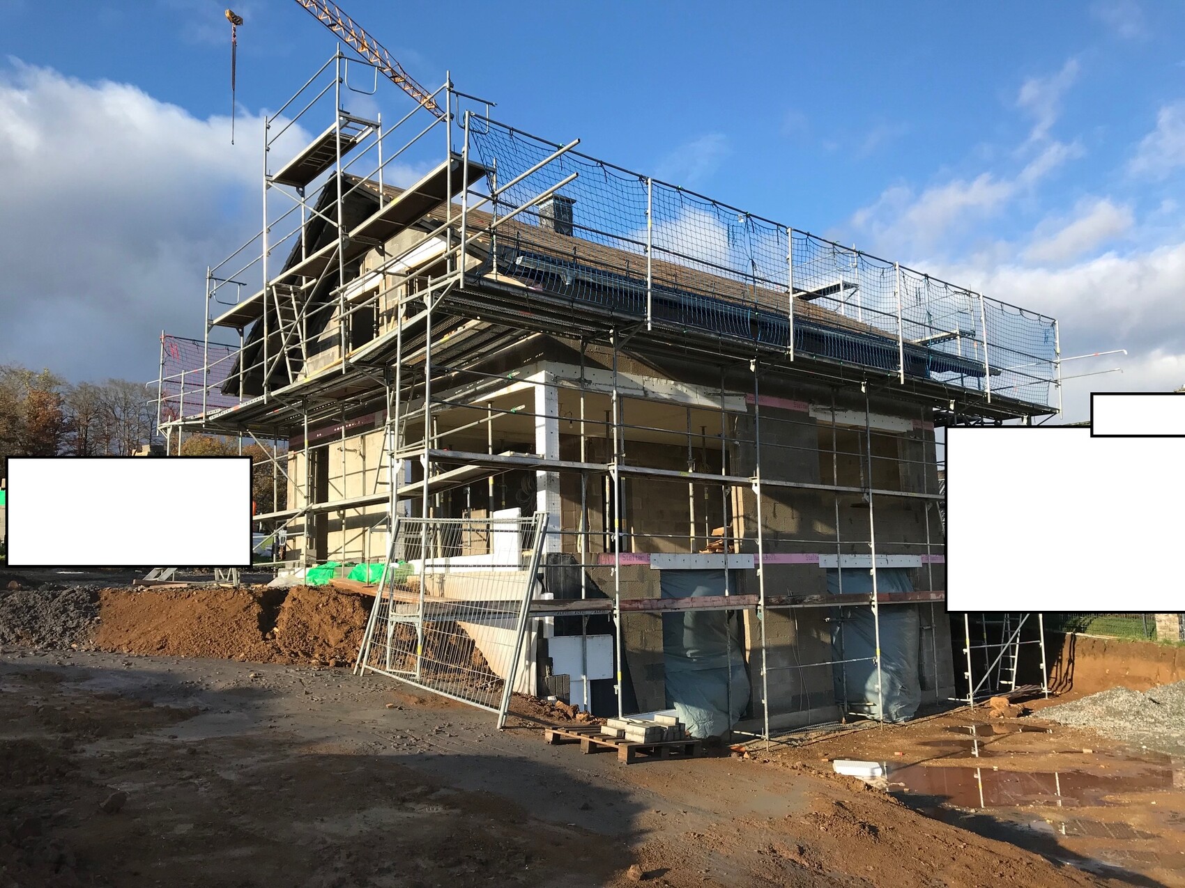 Baustelle mit Baugerüst um Gebäude; Kran im Himmel, Schlamm und Materialien.