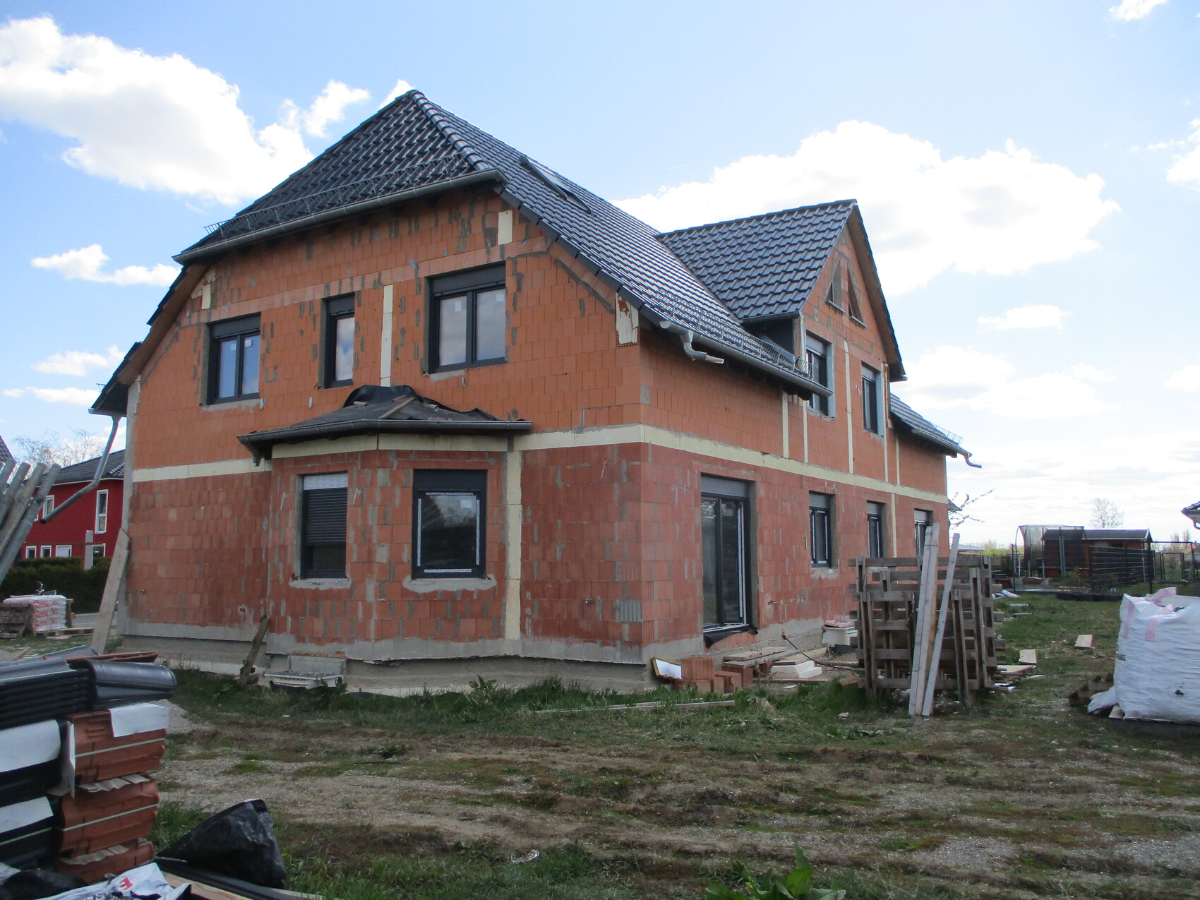 Neubau eines roten Ziegelhauses im Rohbau; Fenster vorhanden, Baumaterialien drumherum.