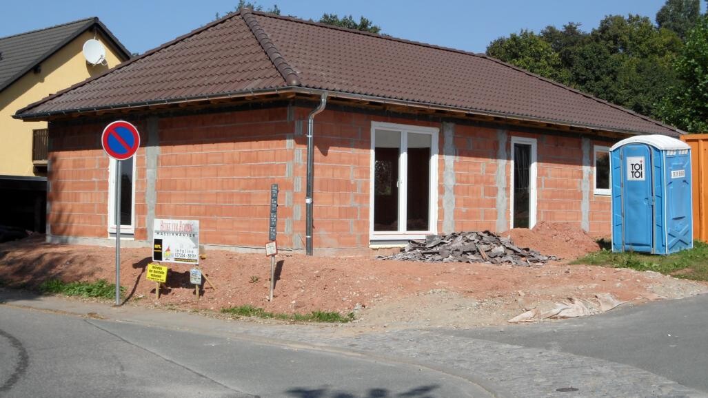 Rohbau eines Einfamilienhauses aus Ziegelsteinen, Bauschutt, rechts blaue Porta-Potti.