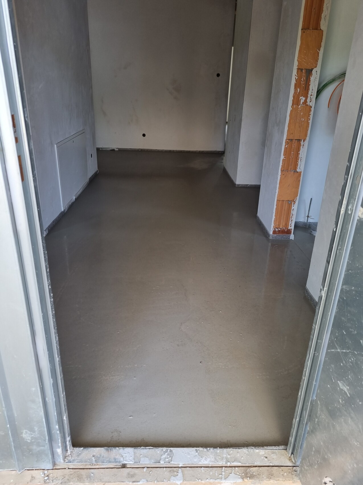 Rohbau-Korridor mit glattem Betonboden; rechte Ziegelstütze und unfertige Wände.