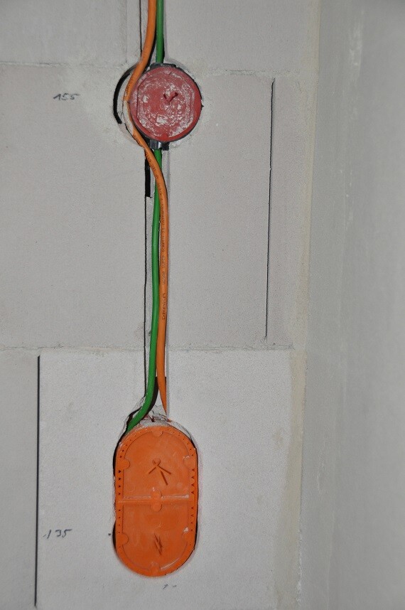Rohbau-Szene mit offenen Elektroleitungen (orange/grüne Kabel) und roter Dose.