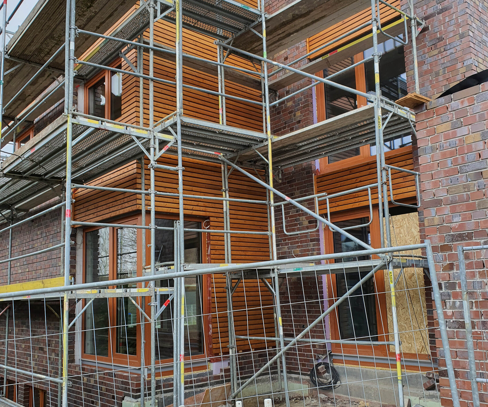 Außenansicht eines Baugerüsts am Backsteingebäude mit orangenen Fensterrahmen.