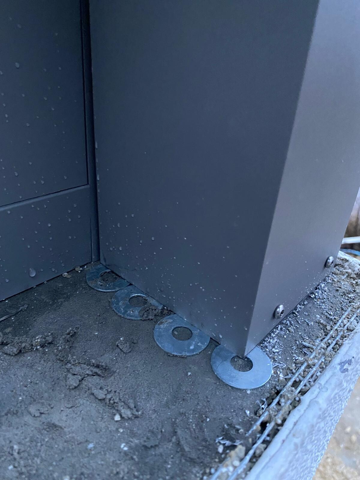 Nahaufnahme einer grauen Metallkonstruktion mit runden Bodenplatten als Bodenanker auf dem Erdboden.