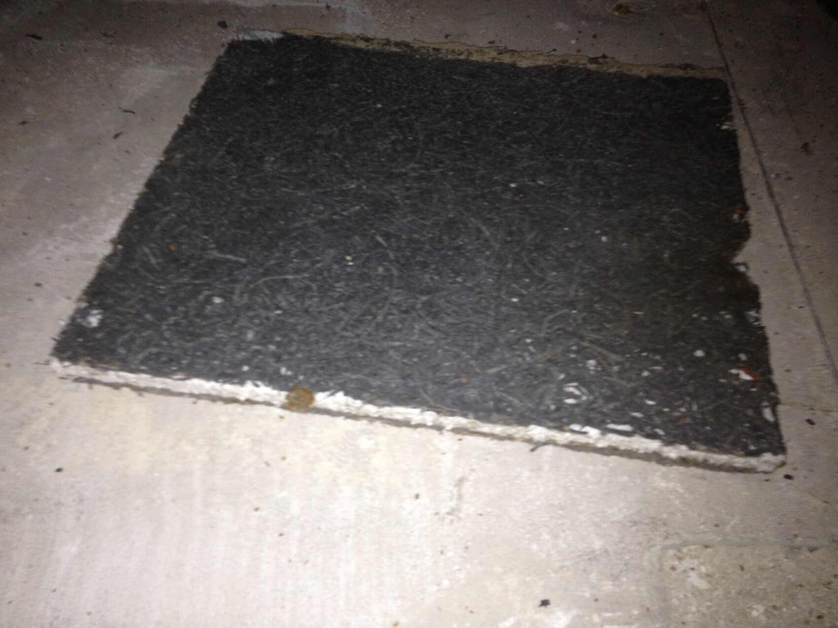 Großes schwarzes Asphaltpatch auf rohem Betonboden in einer Bauumgebung.