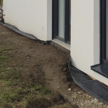 Außenwand eines Gebäudes mit Erdreich neben dem Fundament und Drainagematte sichtbar.