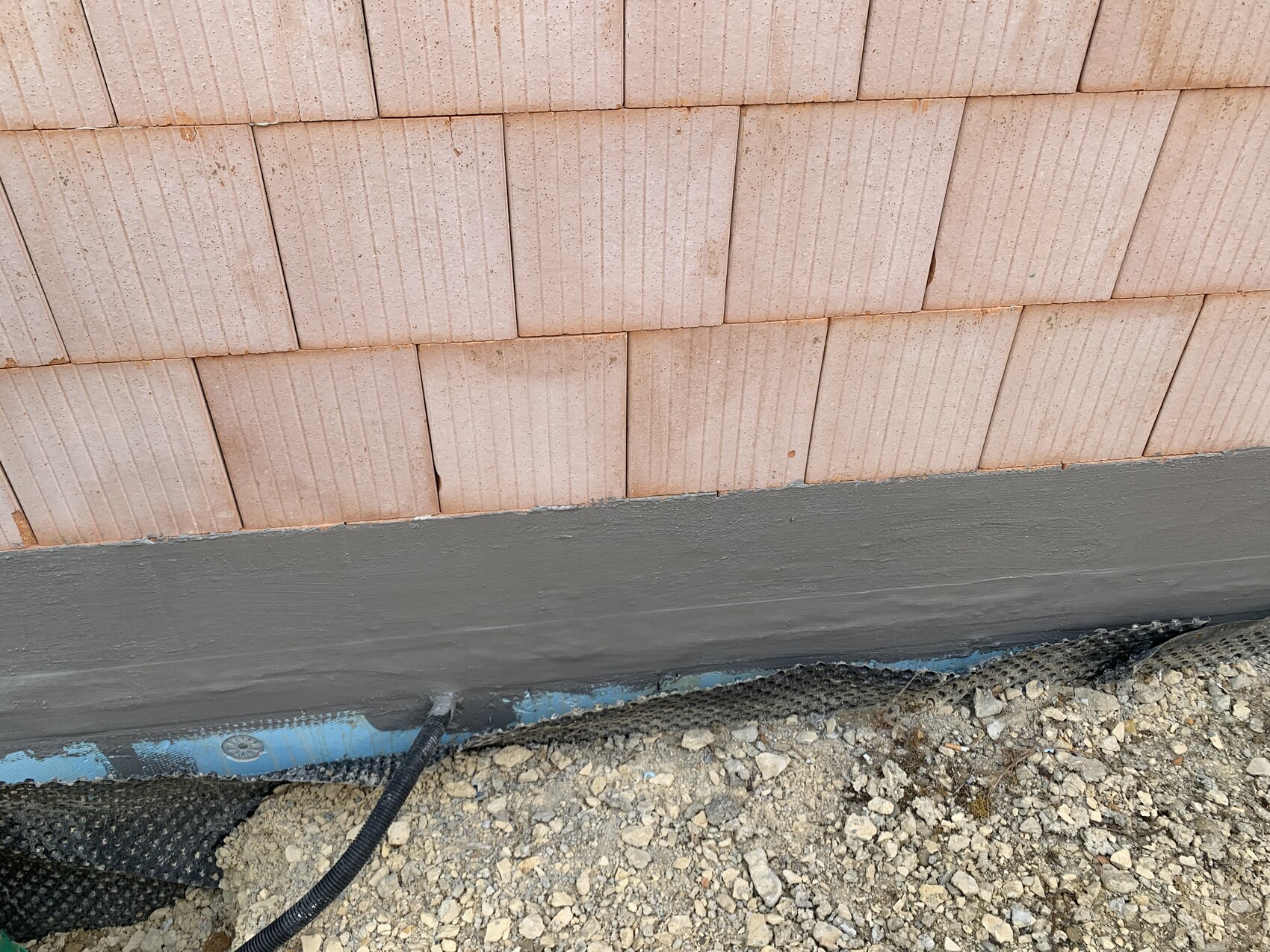 Außenwand aus Ziegeln im Rohbau, Fundamentabdichtung sichtbar, Kiesboden