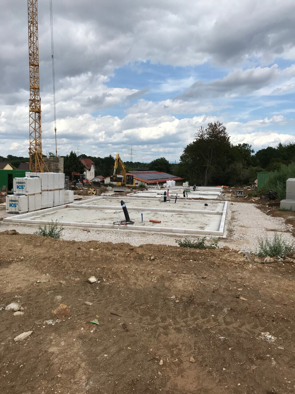 Fundamentplatten-Baustelle mit Kran, Bagger und gestapeltem Baumaterial unter wolkigem Himmel.