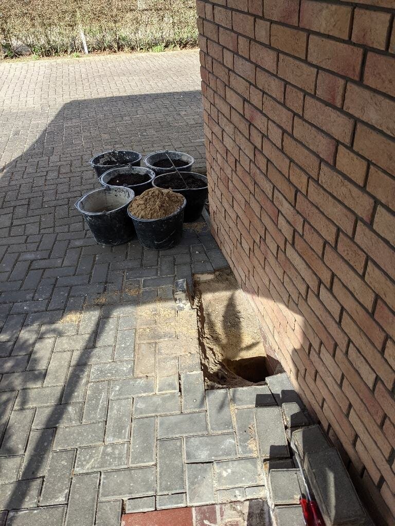 Mehrere Eimer Sand neben einer Baugrube an einer Backsteinwand auf gepflastertem Boden.