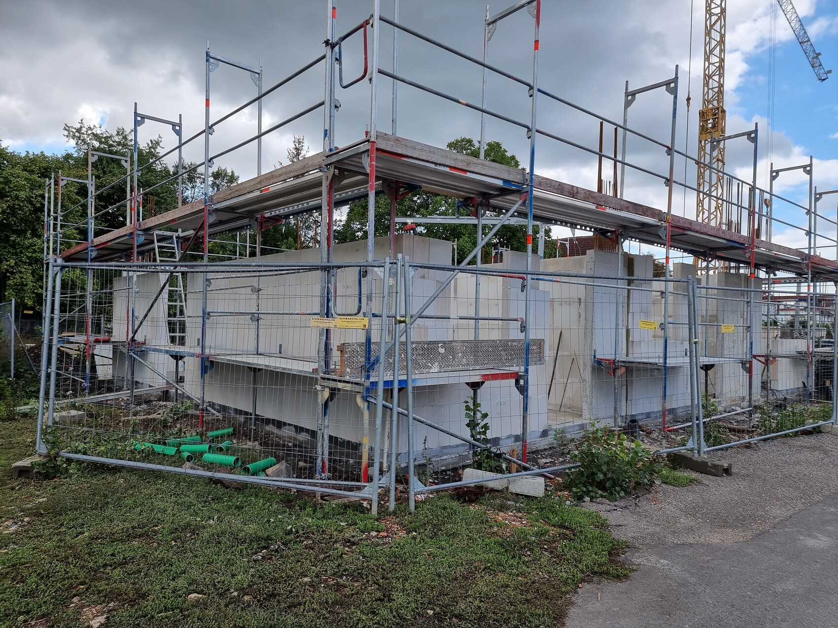 Baustelle mit Gerüst um Betonbau, Bauzäune, Kran im Hintergrund.