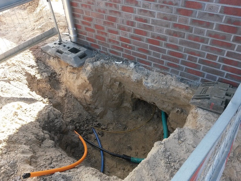 Aushubgrube neben Hauswand mit Bauleitungen und Grundleitungen an einer Baustelle