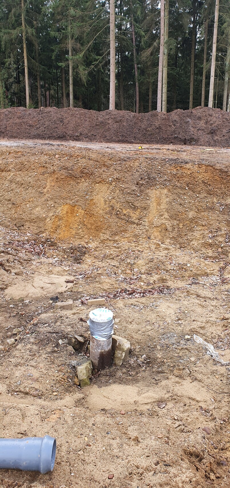 Baugrube mit Rohrinstallation und Erdreich, Wald im Hintergrund