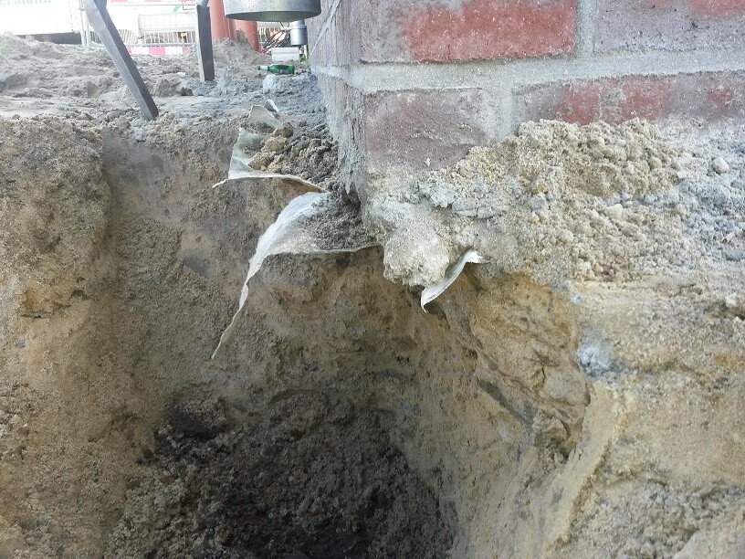 Offene Baugrube neben Fundamentmauer aus Ziegeln bei Bauarbeiten.