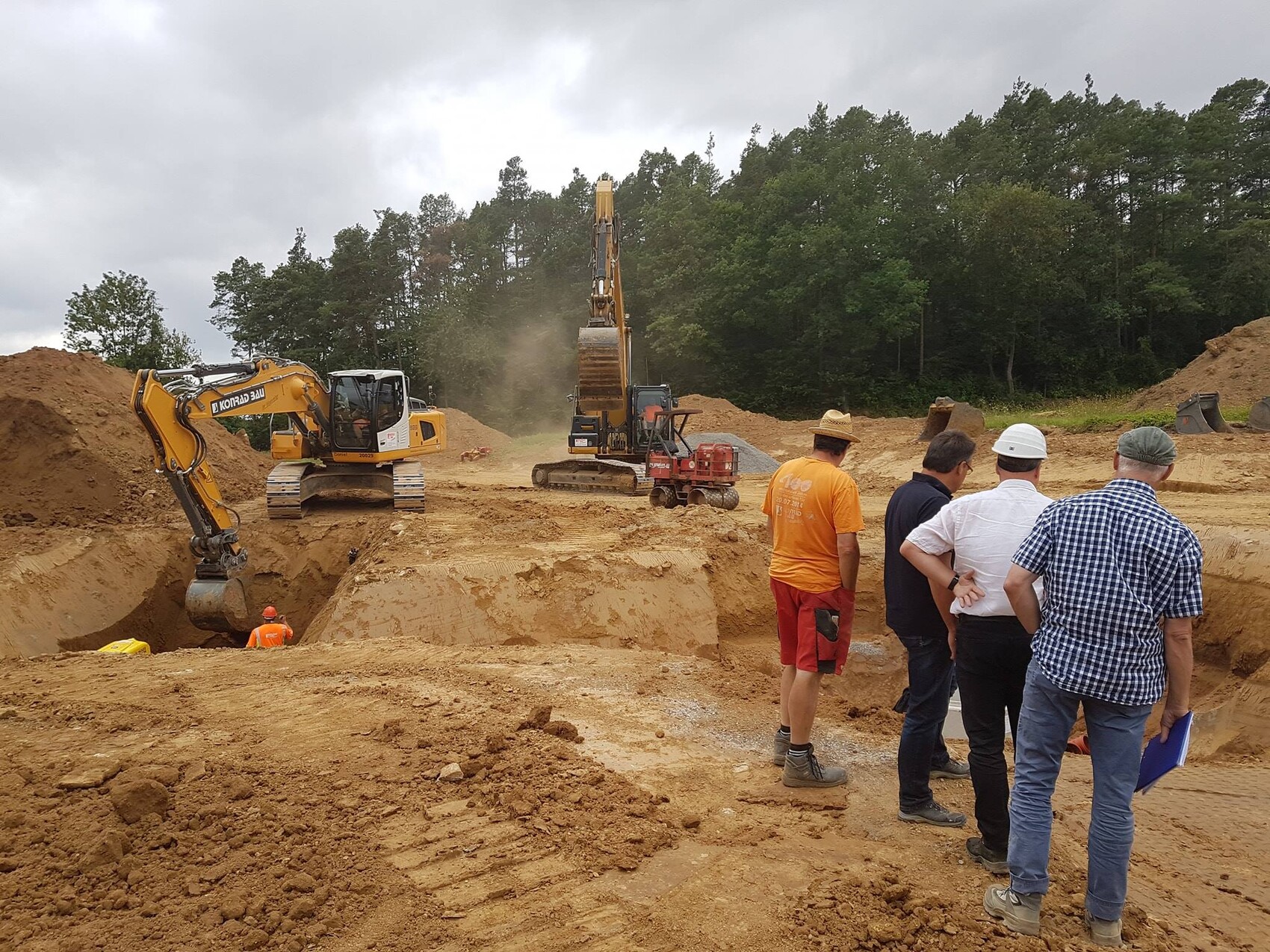 Baustelle mit Baggern, Graben, Arbeiter, Wald im Hintergrund bei Fundamentarbeiten
