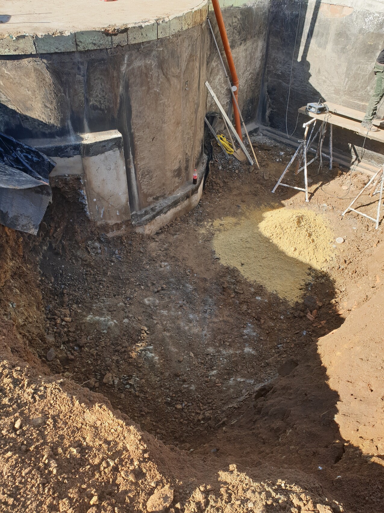 Rundes Betonbecken in einer Baugrube, Aushub, Werkzeuge, Sandhaufen und Stative.