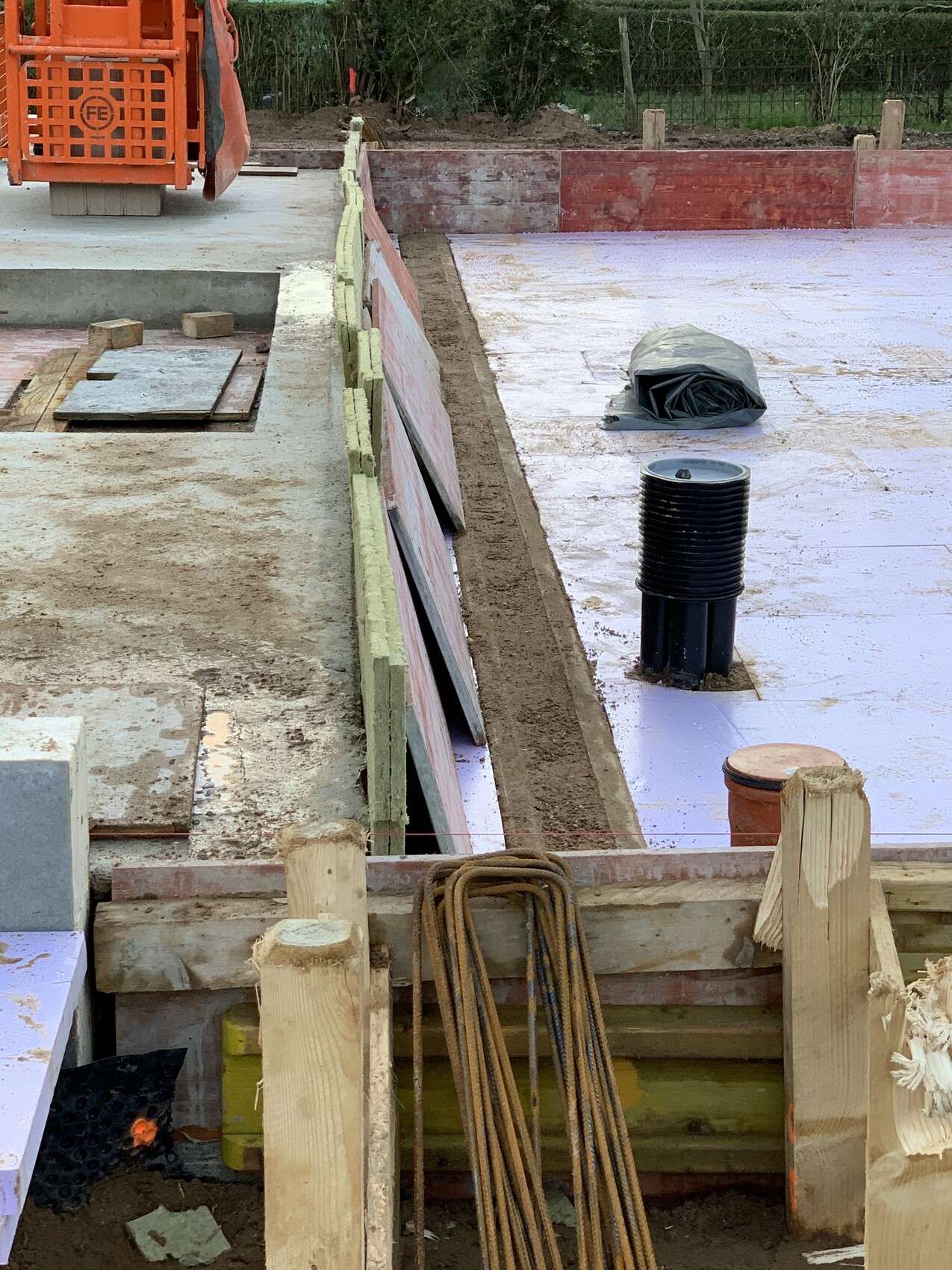 Baustelle: Fundamentform mit Holzrahmen, Dämmplatten und schwarzem Rohr.