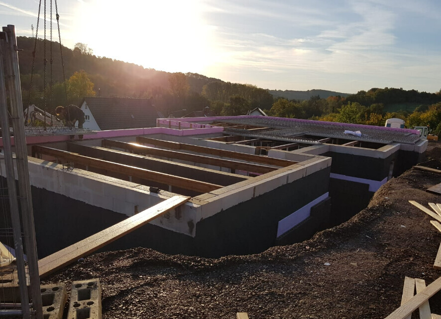 Betonfundamente mit Holzformen auf einer Baustelle im Abendlicht, Hanglage.