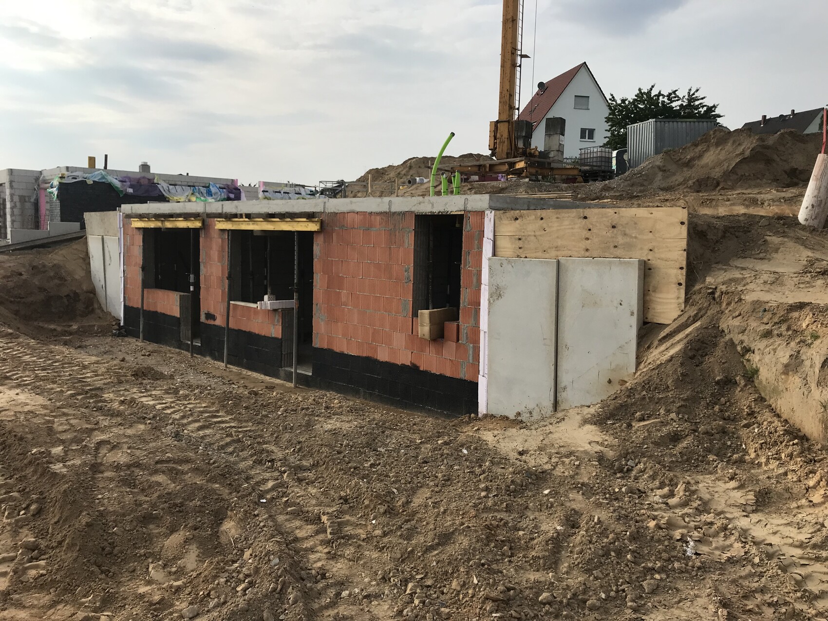 Rohbaufundament aus roten Ziegeln, Baugrube, Baugerät und Kran im Hintergrund