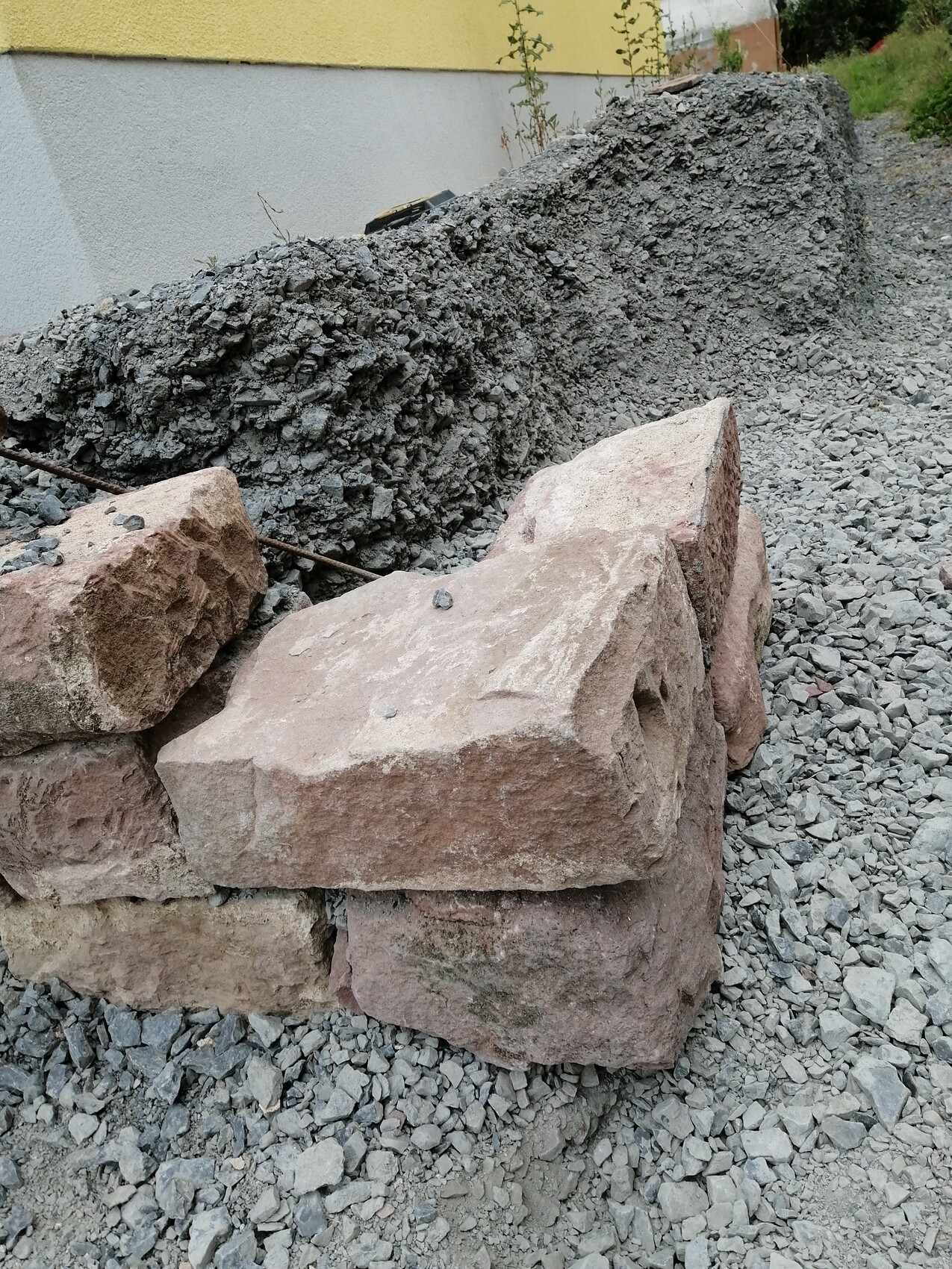 Baustelle mit groben Steinblöcken, Geröll und Kies neben einer Hauswand